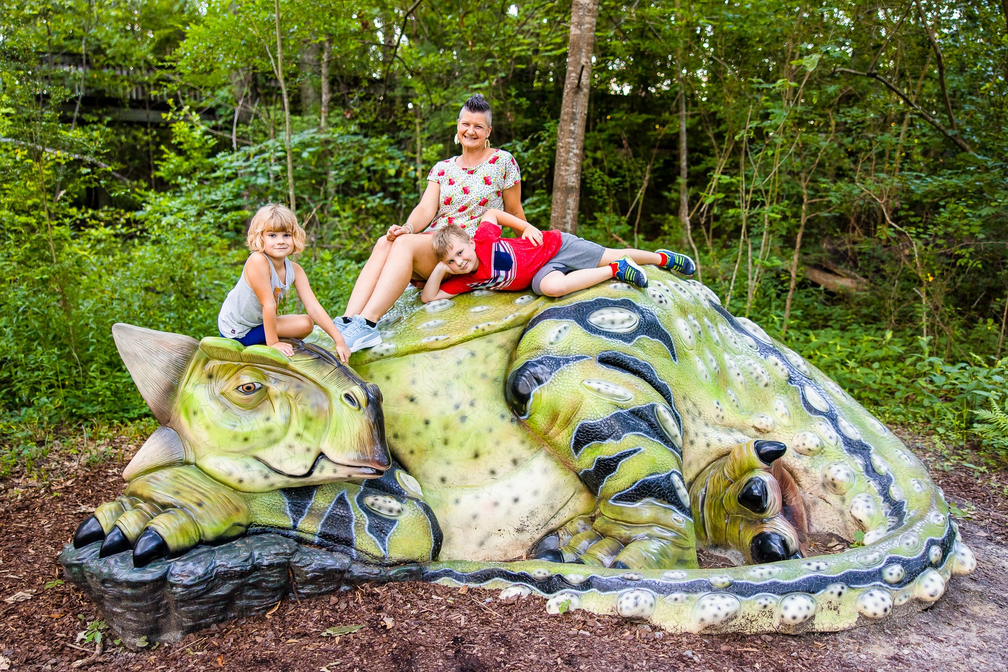 Family sits atop a green dinosaur sculpture